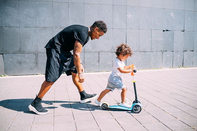 Ein Vater hilft seinem kleinen Sohn beim Rollerfahren
