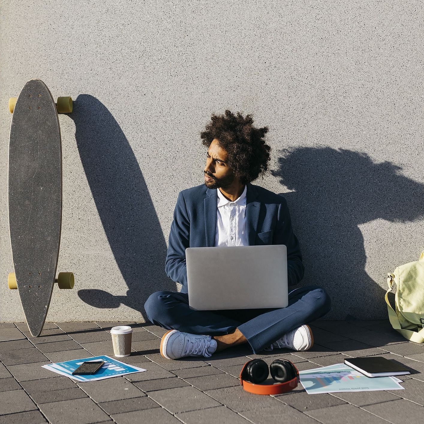 Ein junger Mann sitzt mit dem Laptop in der Hand auf dem Boden. Neben ihm: sein Smartphone
