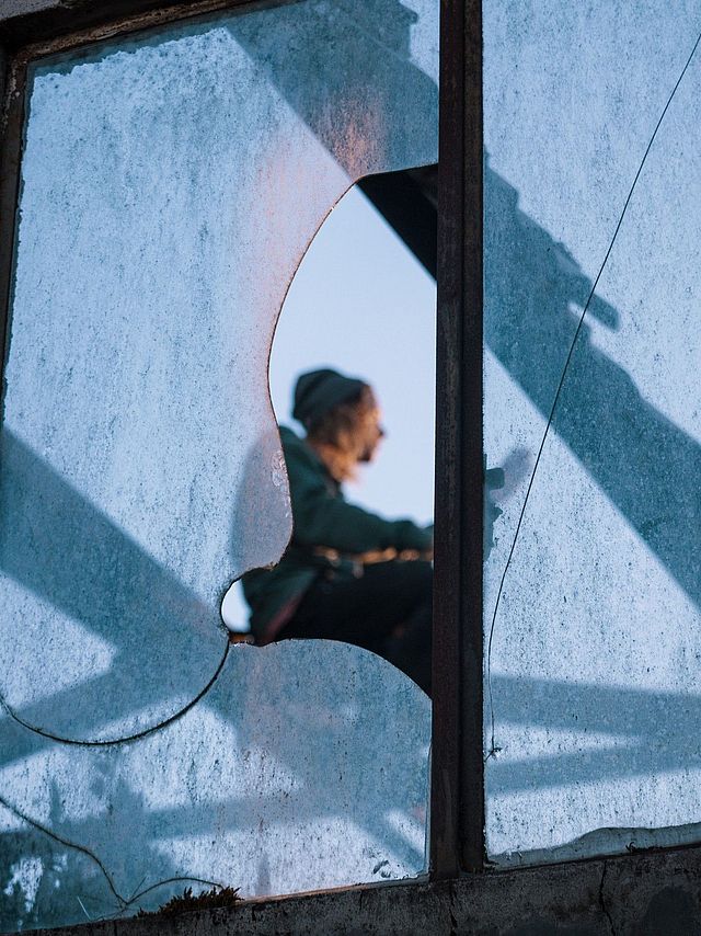 Frau sitzt hinter einer zerbrochenen Fensterscheibe