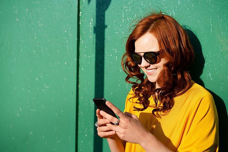 Rothaarige junge Frau mit Smartphone in der Hand