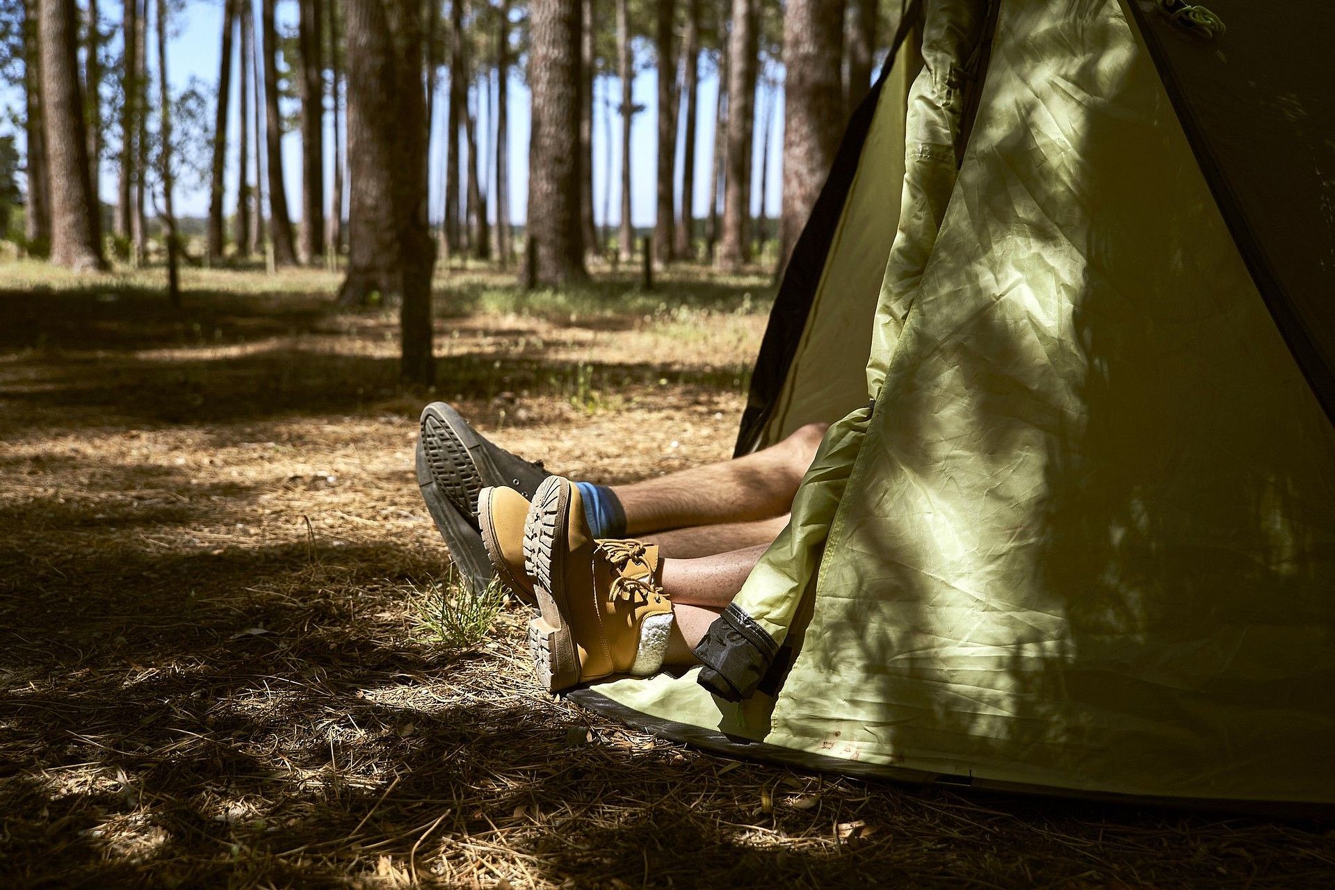 Ein Paar im Wald beim Campen. Aus dem Zelt schauen die Beine