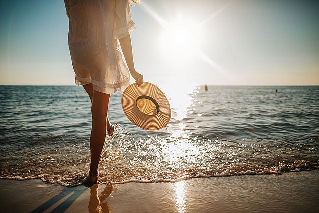 Frau mit Strohhut und weißem Kleid am Strand