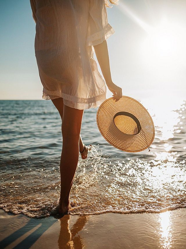 Frau mit Strohhut und weißem Kleid am Strand
