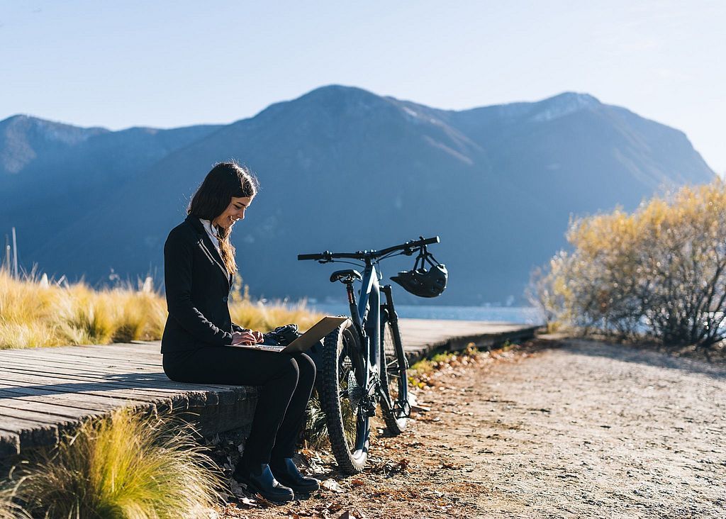 Frau mit Laptop und E-Bike vor einem Gebirgssee