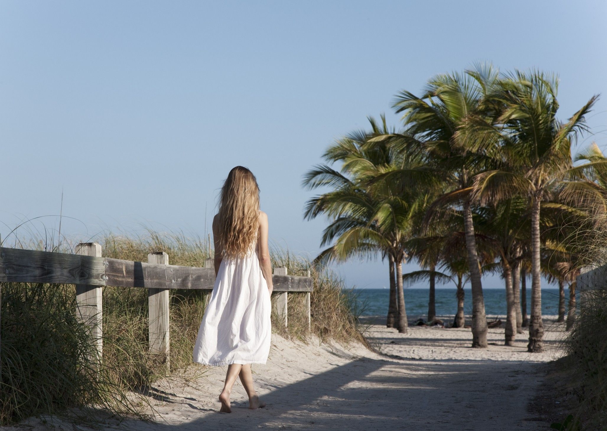 Frau in weißem Sommerkleid auf dem Weg zum Strand